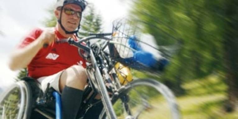 Sportlicher Mann mit Rollstuhlfahrrad rollt mit Geschwindigkeit eine Straße herunter